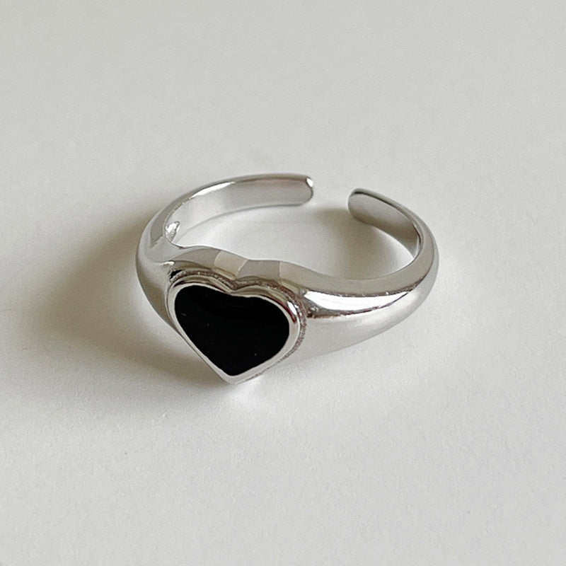 A silver-toned adjustable ring featuring a polished heart-shaped black inlay, photographed on a neutral light gray background.