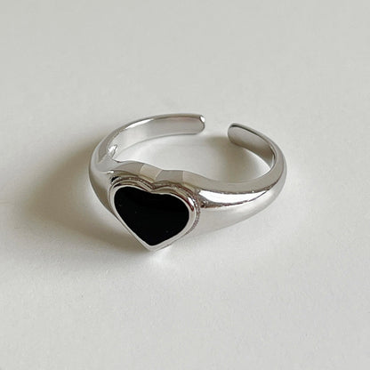 A silver-toned adjustable ring featuring a polished heart-shaped black inlay, photographed on a neutral light gray background.