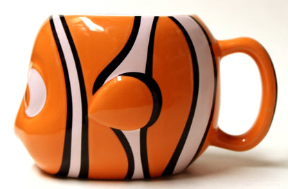 An orange ceramic mug shaped like a clownfish, featuring black and white stripes, a raised eye on the side, and a matching orange handle, shown against a plain white background.