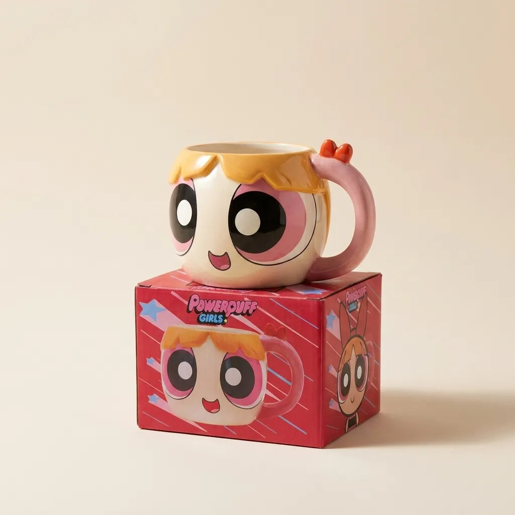 A Powerpuff Girls ceramic mug with a character face and pink handle, displayed on top of its red branded box against a warm beige background.