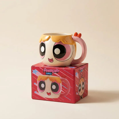 A Powerpuff Girls ceramic mug with a character face and pink handle, displayed on top of its red branded box against a warm beige background.