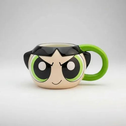 A ceramic mug shaped like a cartoon character's face, featuring a beige skin tone, large black and green eyes, black hair, and a bright green handle, photographed on a light gray studio background.