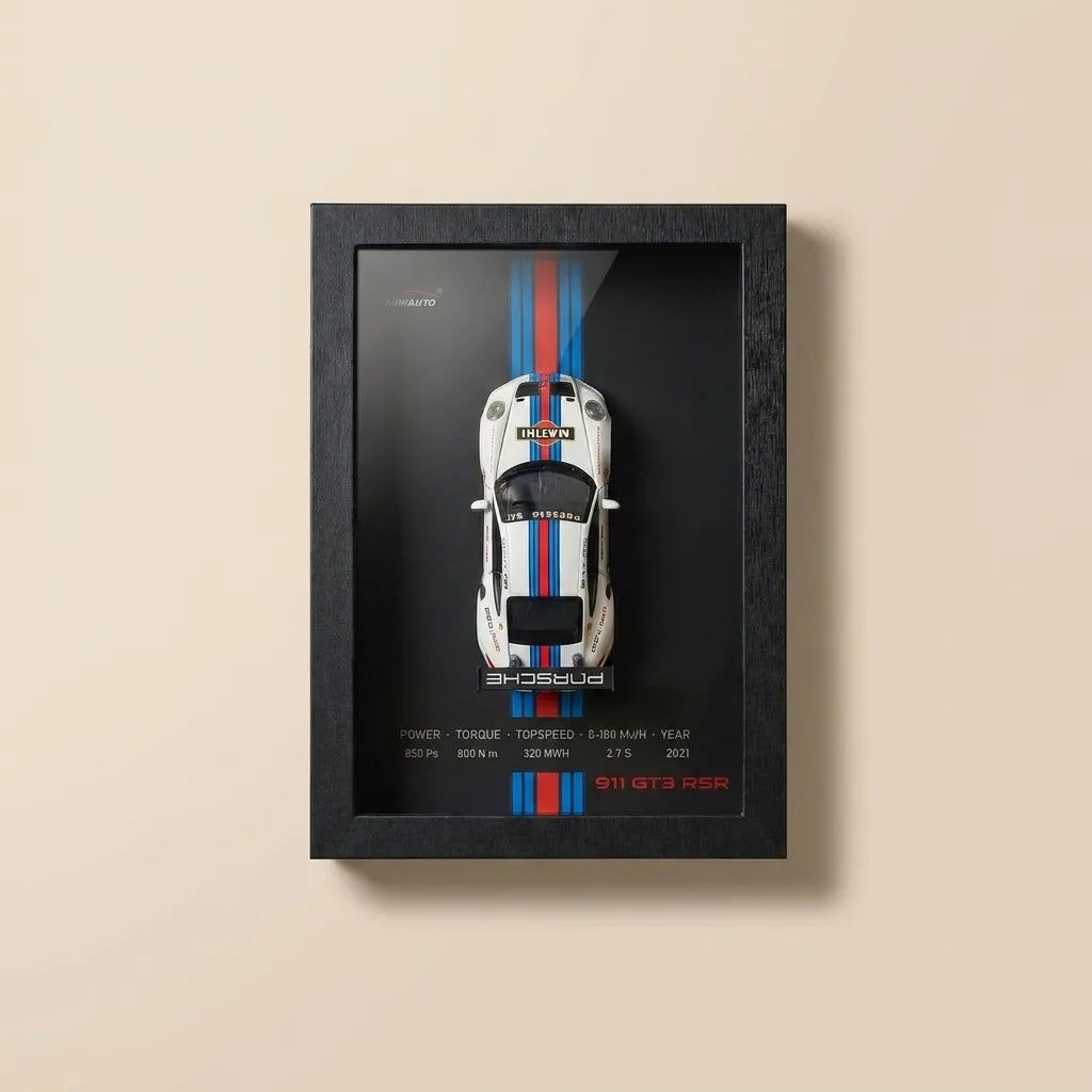 A framed wall art print featuring a top-down view of a white sports car with blue and red racing stripes on a black background, mounted on a beige wall.