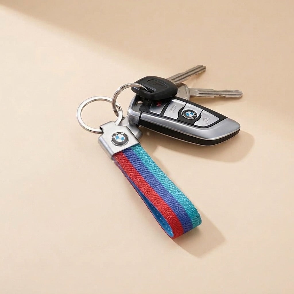 A silver metal keyring holding car keys and a colorful striped fabric keychain strap, set against a warm beige background.