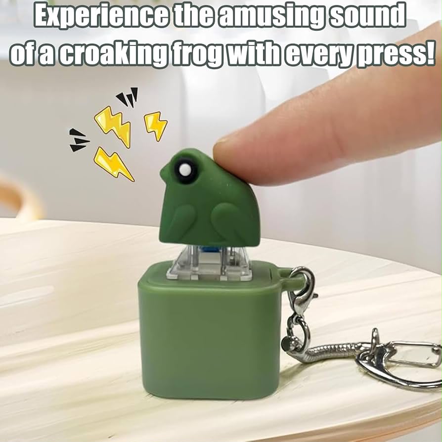 A small green frog-shaped novelty keychain or button on a square base, with a finger pressing the frog. The image includes overlaid text reading 'Experience the amusing sound of a croaking frog with every press!' and yellow lightning-bolt graphics.