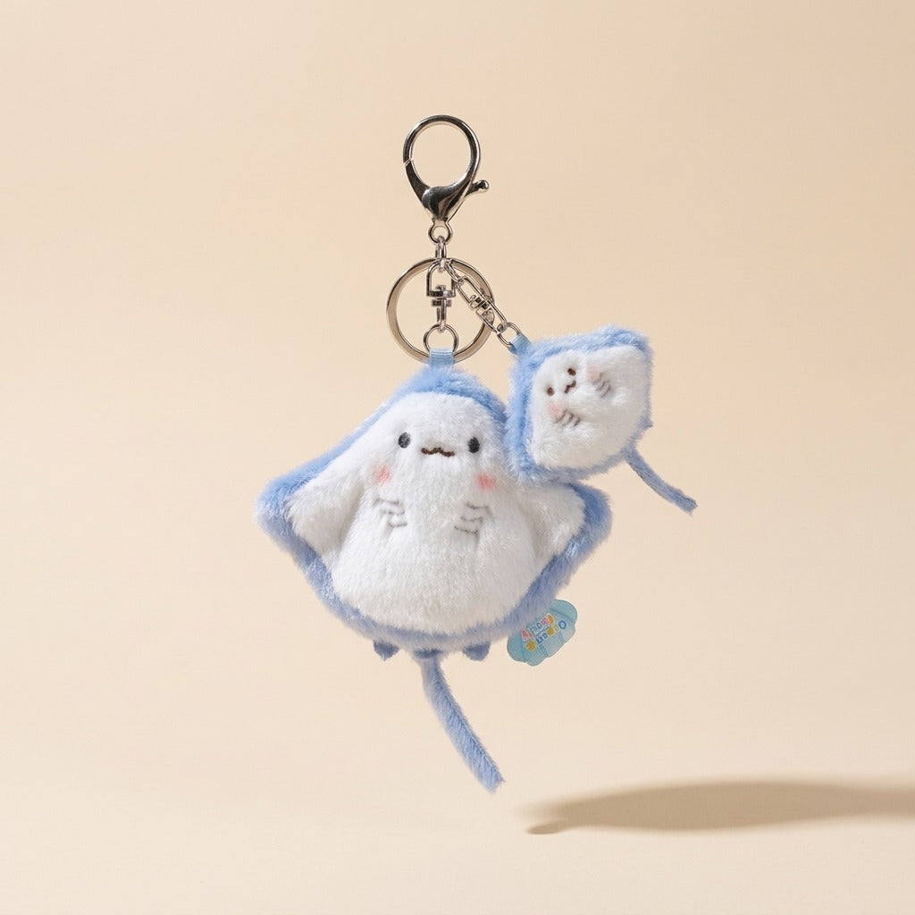 A cute plush keychain shaped like a white cloud with light blue stitched outlines and a small matching cloud charm, attached to a black metal clasp on a warm beige background.