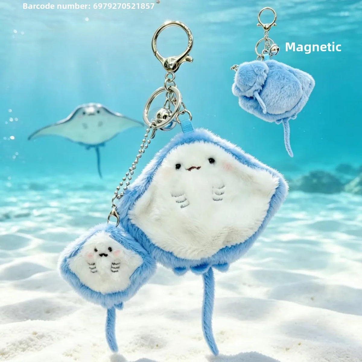 Three plush stingray-shaped keychains in light blue and white with embroidered faces, shown underwater with a sandy seabed and a stingray in the background. One keychain has a metal clasp and chain, and another inset shows a magnetic version.