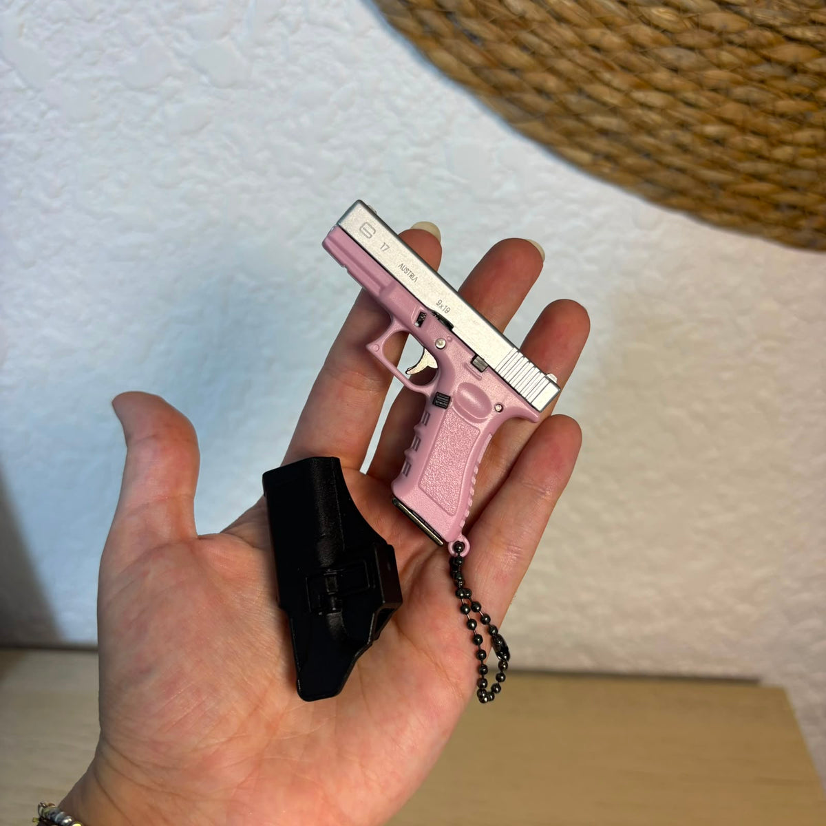 A miniature pink and silver replica handgun keychain held in a person's hand, featuring a black magazine and a black ball chain.