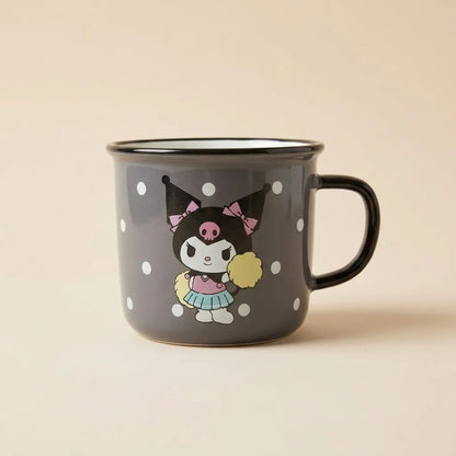 A dark gray enamel-style mug with a black handle and rim, decorated with white polka dots and a cartoon character holding a yellow pom-pom, on a warm beige background.