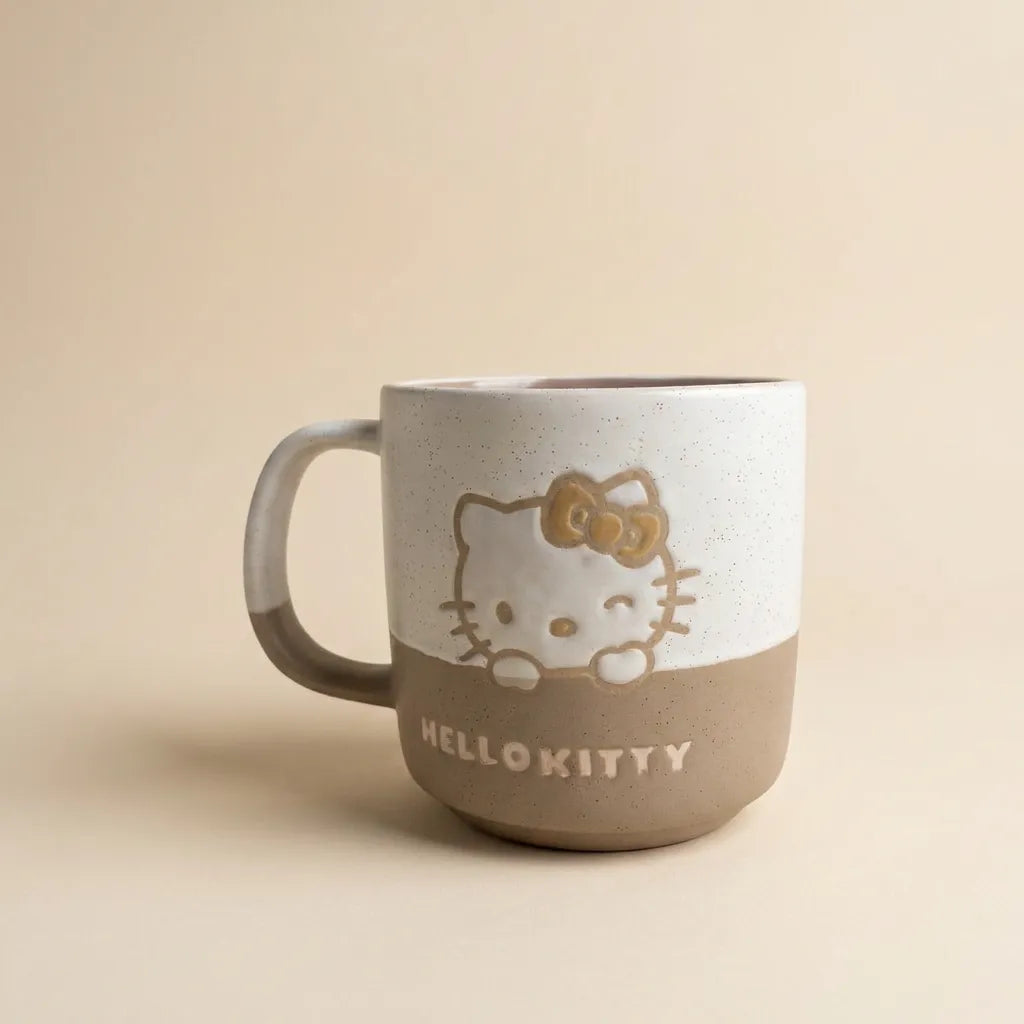 A ceramic Hello Kitty mug with a two-tone design, featuring a speckled off-white top half and a matte taupe-brown bottom half. The character is depicted peeking over the edge, with 'HELLO KITTY' printed in white on the brown section.