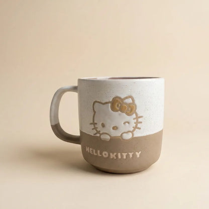 A ceramic Hello Kitty mug with a two-tone design, featuring a speckled off-white top half and a matte taupe-brown bottom half. The character is depicted peeking over the edge, with 'HELLO KITTY' printed in white on the brown section.