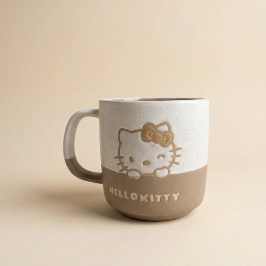 A ceramic Hello Kitty mug with a two-tone design, featuring a speckled off-white top half and a matte taupe-brown bottom half. The character is depicted peeking over the edge, with 'HELLO KITTY' printed in white on the brown section.