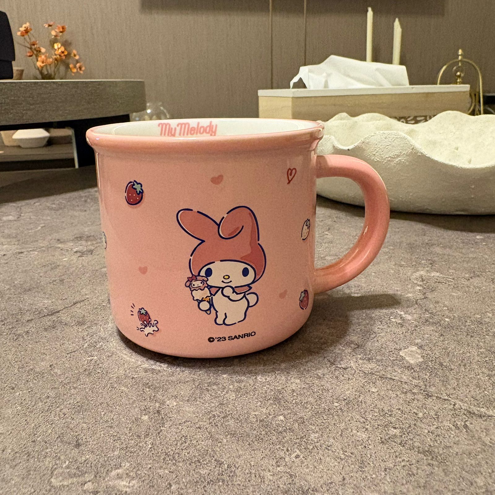 A pink ceramic mug featuring Sanrio's My Melody character, shown on a gray stone countertop in a home setting.