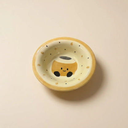 A small hand-painted ceramic bowl with a cute coffee cup character printed inside, set against a plain beige background.