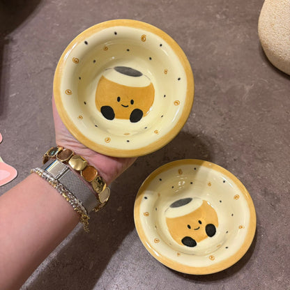 Two small ceramic bowls with a cute cartoon character design, held in a hand over a gray stone surface.