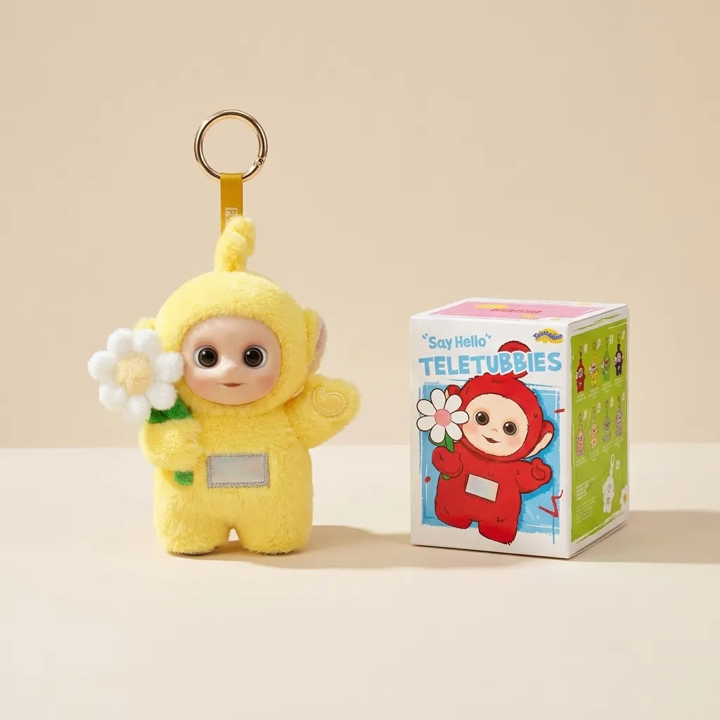 A yellow Teletubbies plush keychain character holding a white flower, shown next to its branded retail box on a warm beige background.