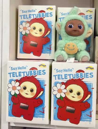 Three 'Say Hello Teletubbies' boxes arranged on a shelf, with a plush Teletubby toy in a mint green outfit placed on top of the right box.