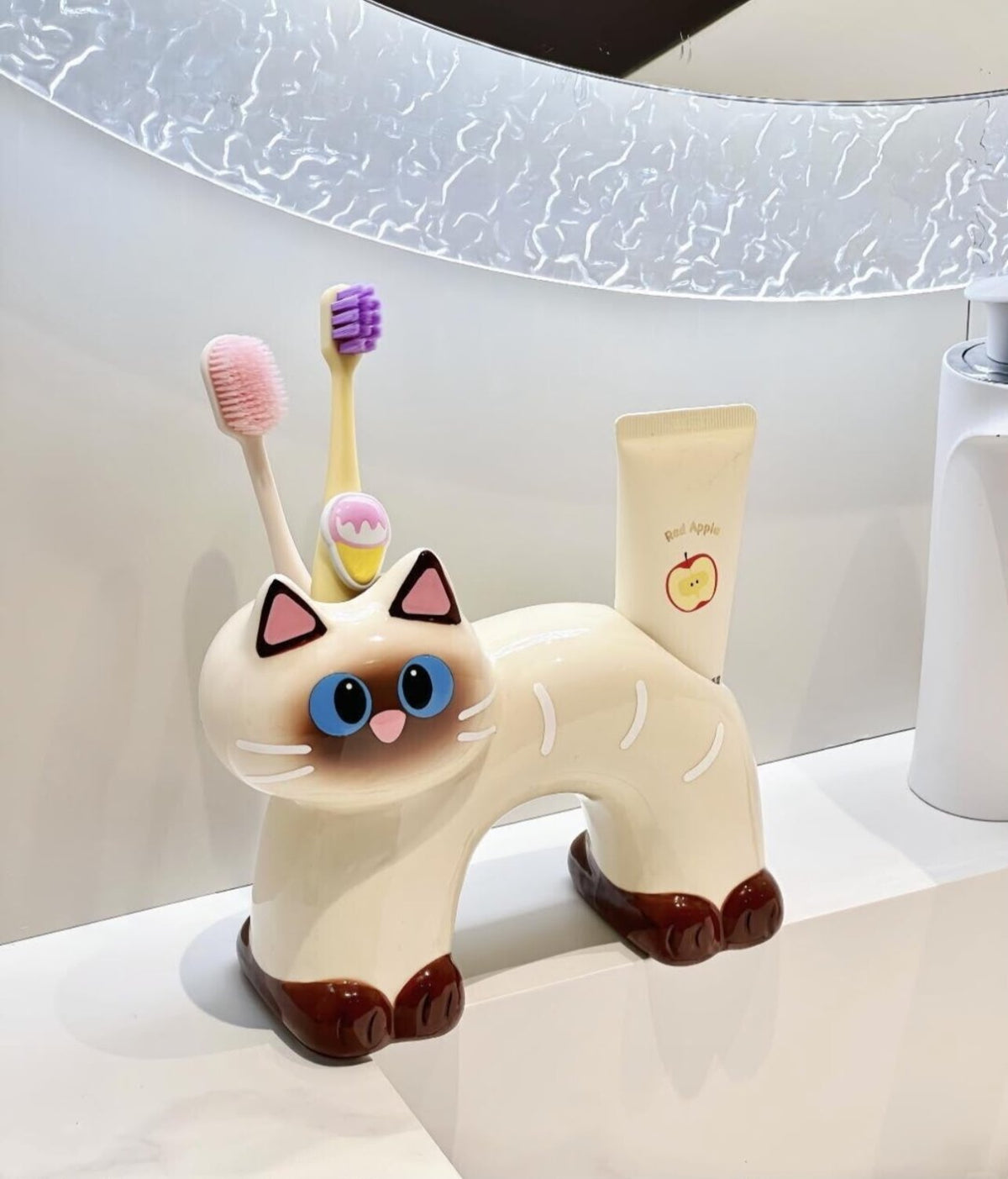Two ceramic cat toothbrush and toothpaste holders in black and cream, sitting on a neutral tabletop.