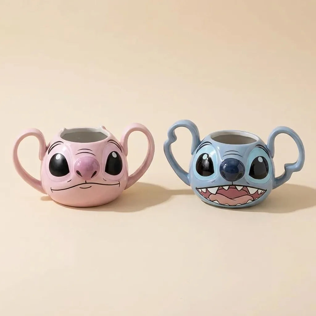 Two cartoon character ceramic mugs shaped like faces, one pink and one blue, each with a handle on the side, displayed on a beige background.