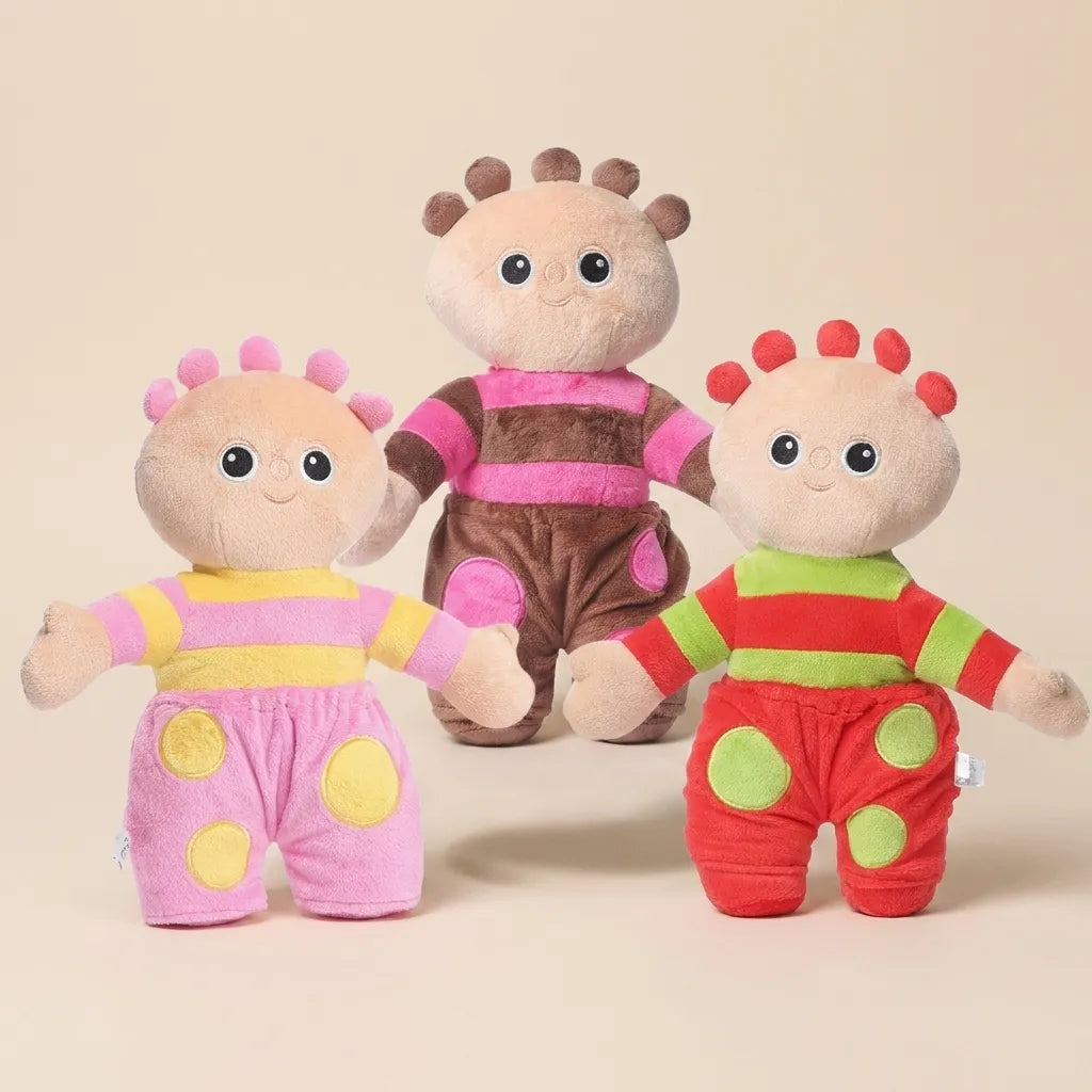 Three plush toy characters dressed in colorful outfits, standing together on a plain beige studio background.