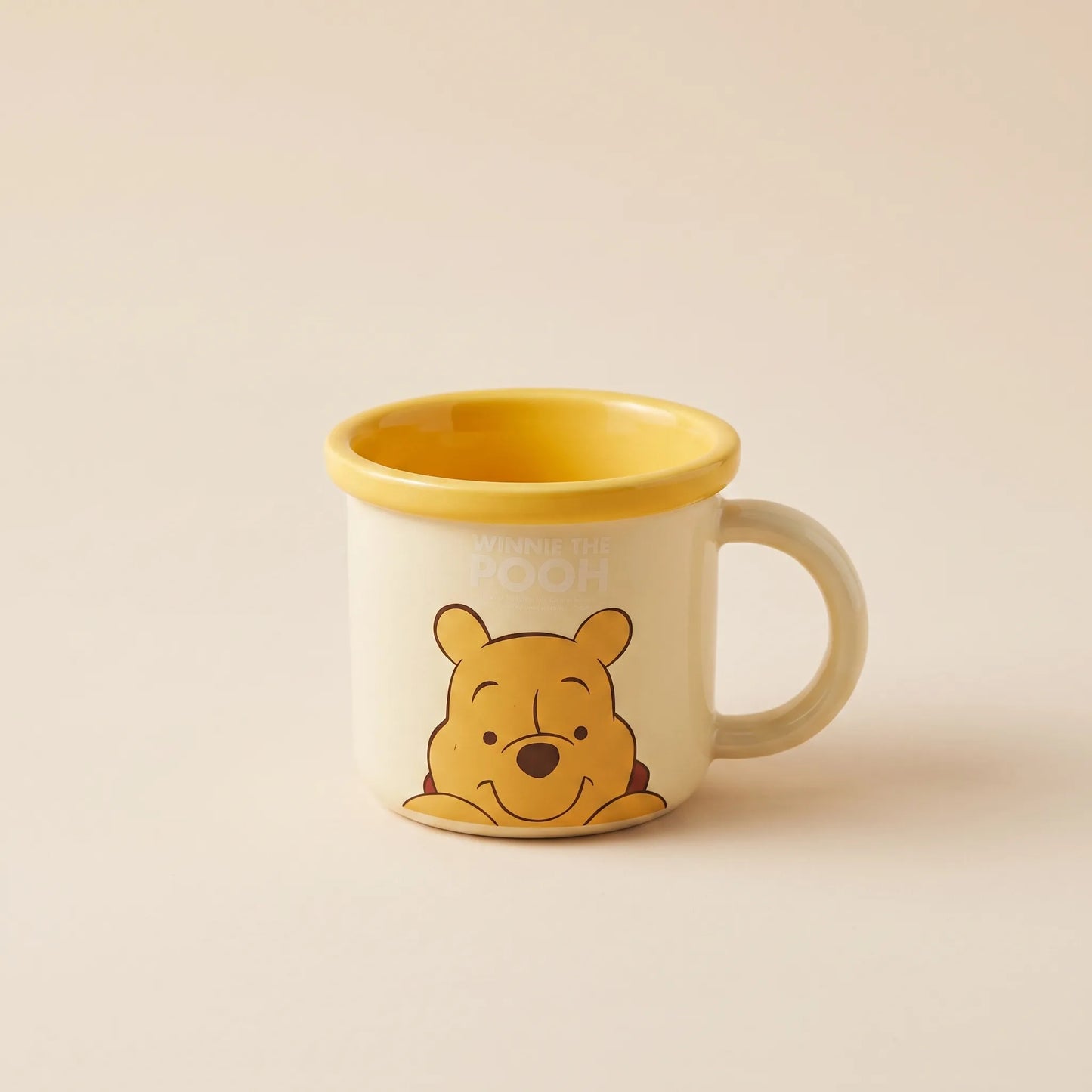 A ceramic mug featuring Winnie the Pooh on the front and a yellow interior, set against a solid beige background.