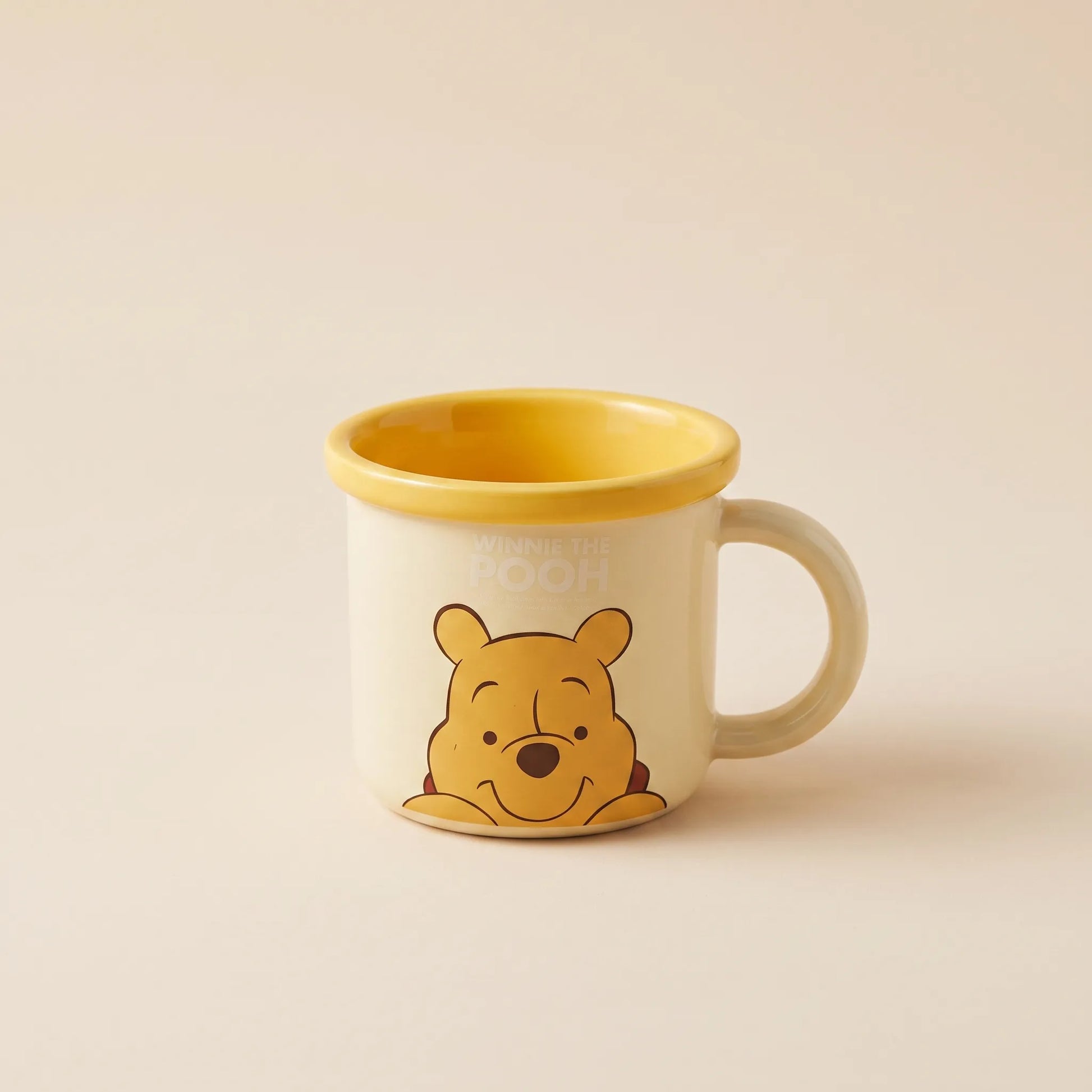 A ceramic mug featuring Winnie the Pooh on the front and a yellow interior, set against a solid beige background.